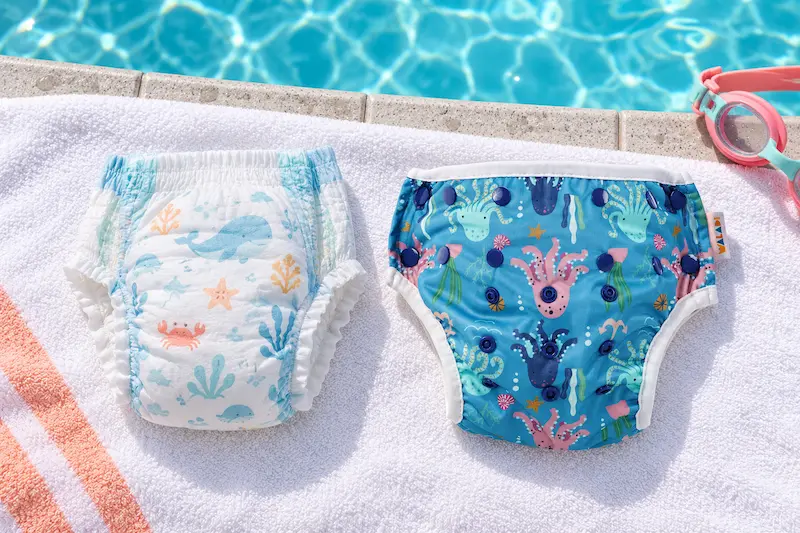 Waladi Octopus Party reusable swim nappy beside a disposable swim nappy on a towel by a swimming pool.
